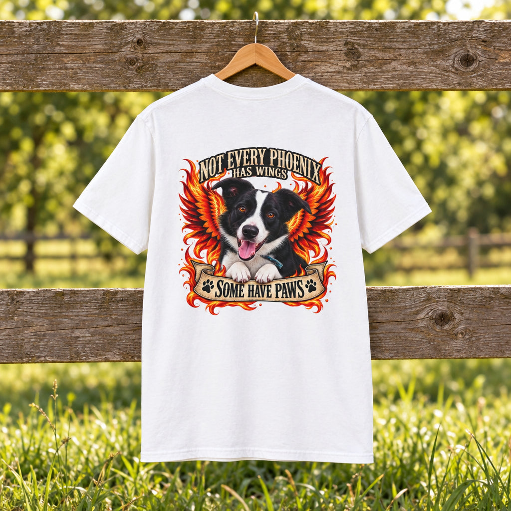 A white short-sleeve t-shirt with a large graphic print on the front, featuring a black and white dog with red and orange wings, flames, and the text 'NOT EVERY PHOENIX HAS WINGS' and 'SOME HAVE PAWS'.